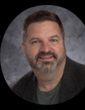 Picture of man with brown hair and brownand grey beard smiling.